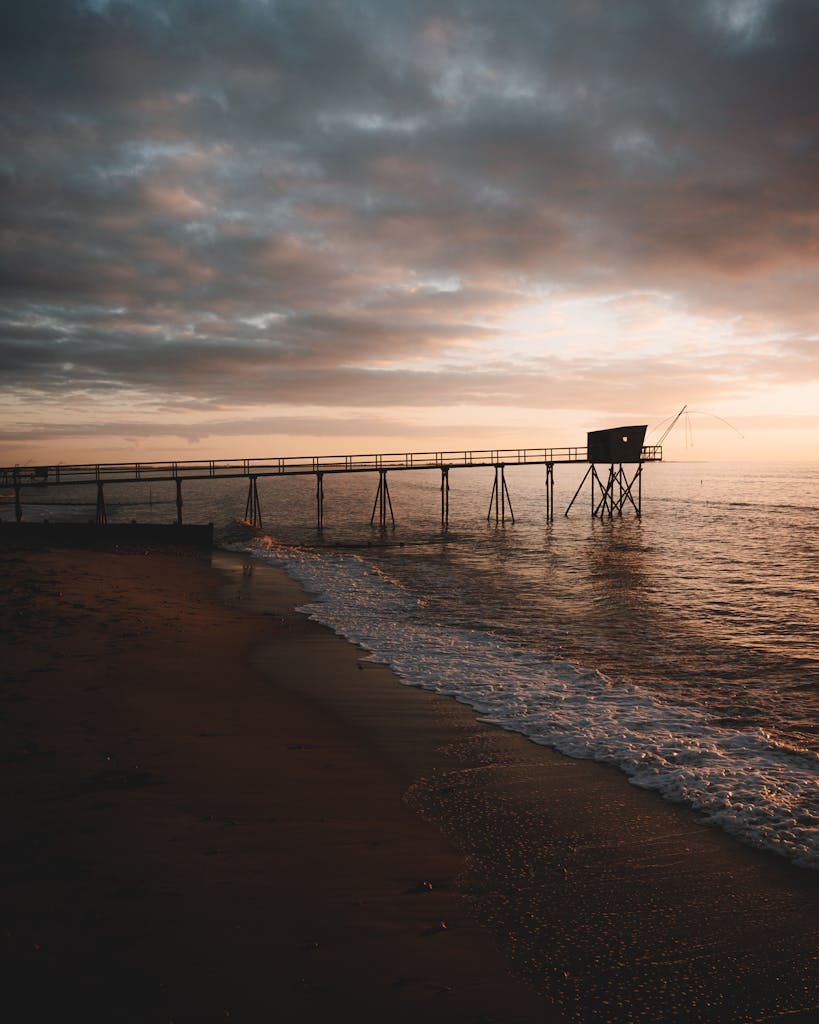 A tranquil seaside view of a pier extending into the sea at sunset in Les Moutiers-en-Retz, France.